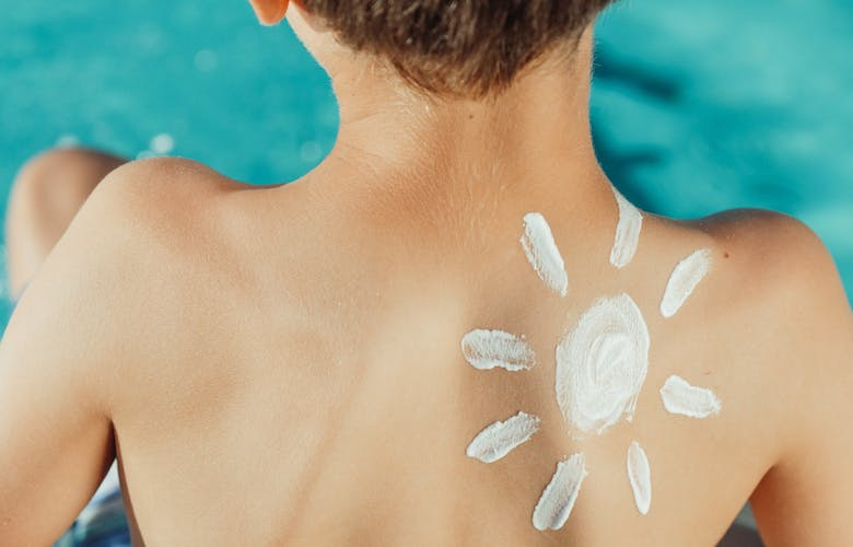 Kind vor Whirlpool mit einer Sonne aus Sonnencreme auf dem Rücken
